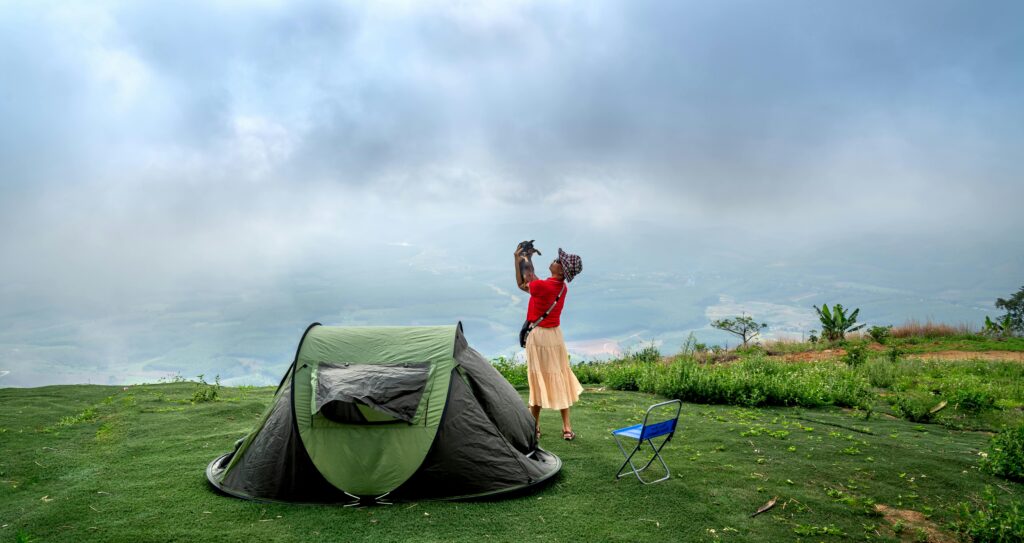 Woman camping with her dog in a scenic mountain landscape under a cloudy sky.