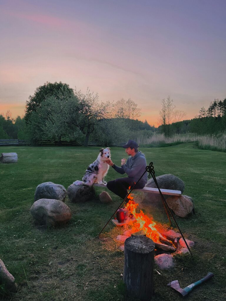 A man sitting with his dog by a campfire in a serene outdoor setting at twilight.